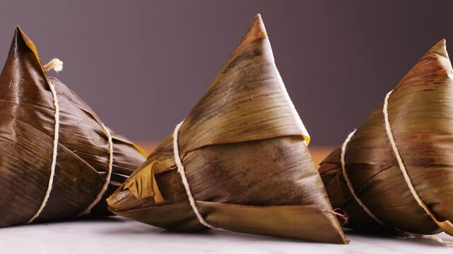Hand holding zongzi (rice dumpling) with savoury fillings wrapped in bamboo or reed leaves.
