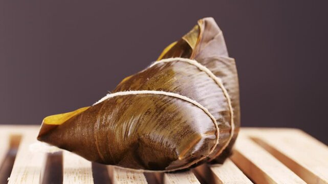 Hand holding zongzi (rice dumpling) with savoury fillings wrapped in bamboo or reed leaves.