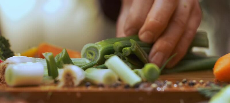 Extreme close-up view of a man chef chopping green onions with sharp knife on wooden slicing board
