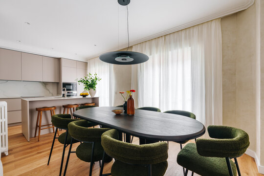 A modern dining area with a dark oval table and six green chairs