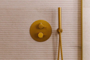 A modern shower fixture with two round, gold knobs on a textured wall