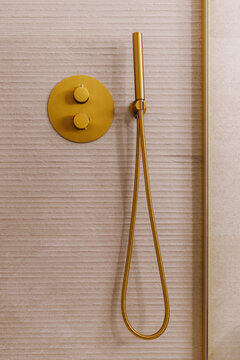 A gold-colored shower fixture with a hose and circular controls