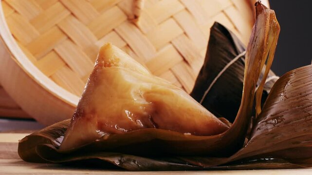 Hand holding zongzi (rice dumpling) with savoury fillings wrapped in bamboo or reed leaves.