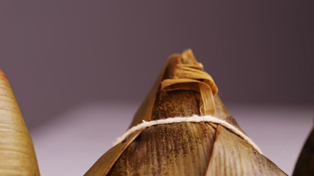Hand holding zongzi (rice dumpling) with savoury fillings wrapped in bamboo or reed leaves.