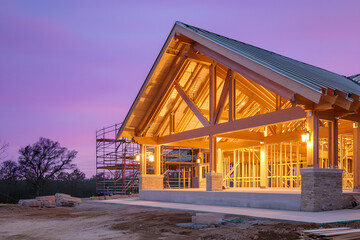 Obraz premium timber frame home under construction at dusk, roof trusses outlined against purple sky