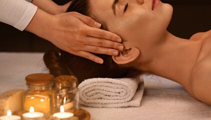 Relaxed young woman getting head massage at romantic spa atmosphere, side view
