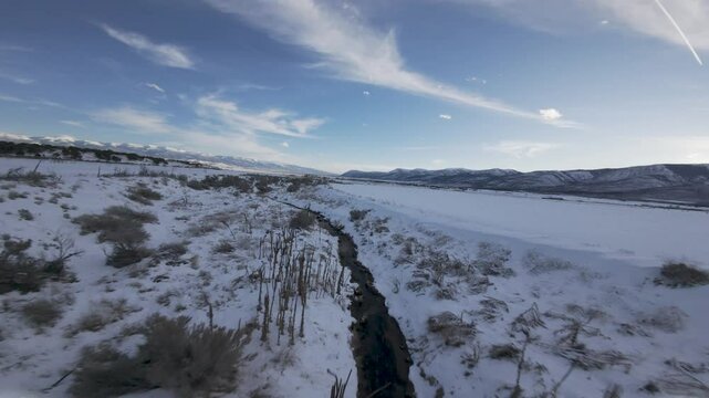 Aerial-FPV-First person view-Flying low and fast over small snow lined stream in the shade of the sun just gone down-high wispy clouds in dark blue sky-cold winter scene