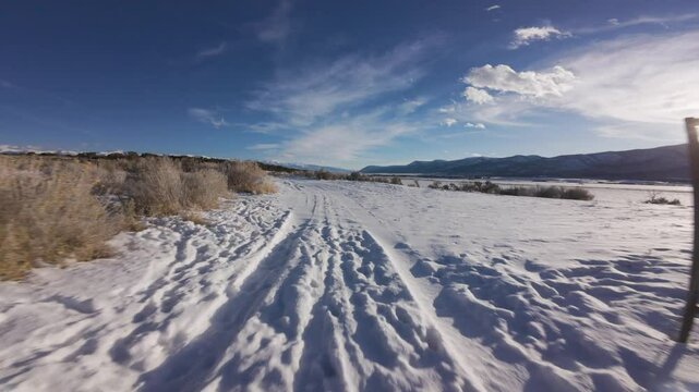 Aerial-First person view-FPV- Flying through open gate-Low over snowy sagebrush lined country lane toward dark blue sky 