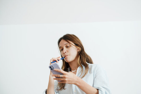 Woman Looks at Her Phone Screen  While Brushing Teeth