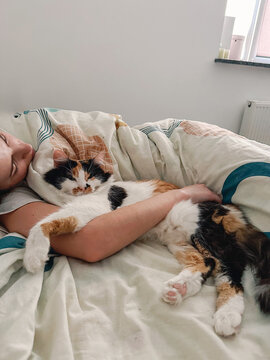 UGC shot of woman sleeping under blanket and hugging her calico cat 