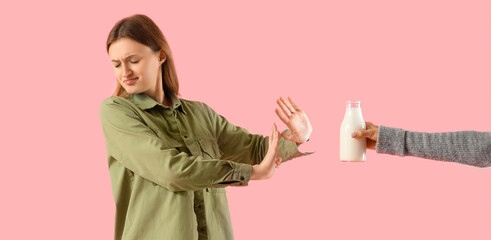 Displeased woman with lactose intolerance rejecting milk on pink background