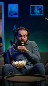 Vertical video Man in apartment chocking on food while watching movie on TV and eating popcorn. Person getting throat clogged while swallowing snack, doing heimlich maneuver on couch, fighting for his