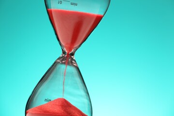 Hourglass with red flowing sand on turquoise background, closeup. Space for text