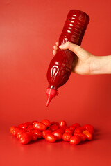Woman squeezing ketchup from bottle over tomatoes on red background, closeup