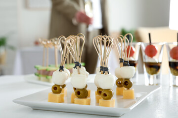 Many different tasty canapes on white table. Woman with glass of wine indoors, closeup