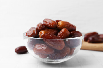 Tasty dried dates in glass bowl on white table, closeup