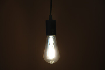 Glowing light bulb hanging on dark background