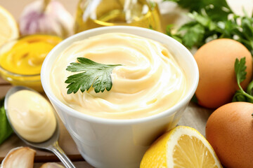 Delicious mayonnaise sauce in bowl and ingredients on table, closeup