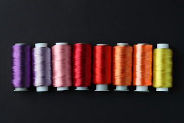 Spools of colorful sewing threads on black background, flat lay