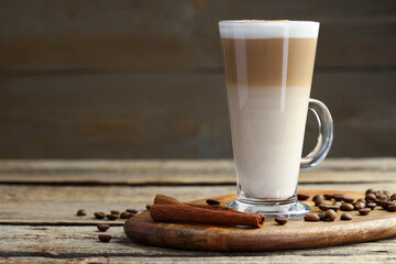 Tasty latte macchiato in glass cup, coffee beans and cinnamon on wooden table, closeup. Space for...