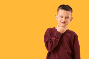 Ill little boy suffering from sore throat on yellow background