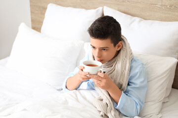 Sick little boy drinking tea in bedroom