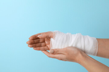 Woman with medical bandage on wrist against light blue background, closeup