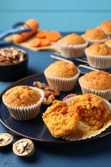 Tasty carrot muffins and walnuts on blue wooden table, closeup