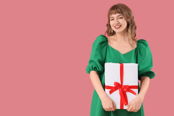 Beautiful young woman with gift box on pink background