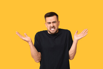 Handsome ashamed young man shrugging on yellow background