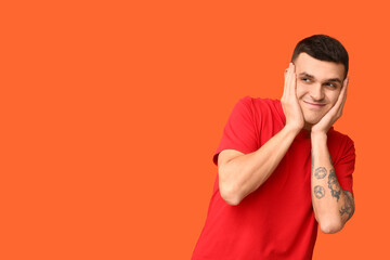 Handsome ashamed young man covering face with hand on orange background