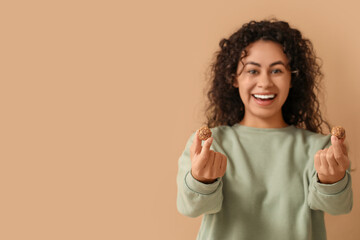 Happy young African-American woman with sweet chocolate candies on brown background