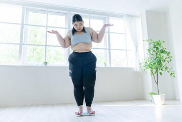 Fototapeta premium 体重計に乗って肩をすくめる女性