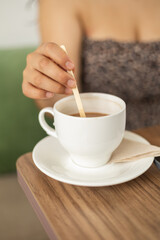 A girl stirs her coffee gently, savoring every swirl, as the warmth of the cup brings comfort and the peaceful atmosphere wraps her in a moment of quiet romance.

