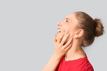 Beautiful young woman suffering from toothache on grey background