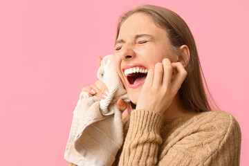 Beautiful young woman suffering from toothache with cold compress on pink background