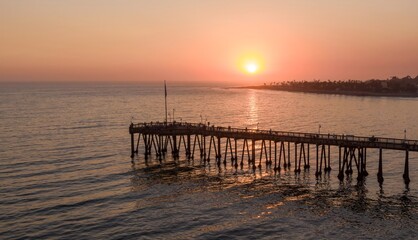Obraz premium People stroll along the pier in Ventura, California, USA, enjoying the sunset. The sun reflects on the water, creating a peaceful and scenic view.