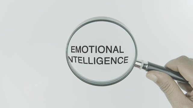 Emotional Intelligence text or word highlighted by a magnifying glass in a hand on a white background, symbolizing self-awareness, emotional regulation, and social skills