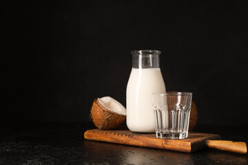 Wooden cutting board and bottle of tasty fresh coconut milk on black background