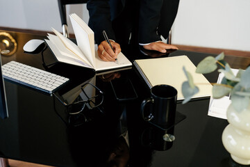 Crop businesswoman taking notes in notebook at office desk