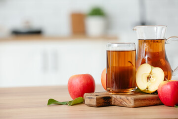 Glass and jug of fresh apple juice on wooden table in kitchen