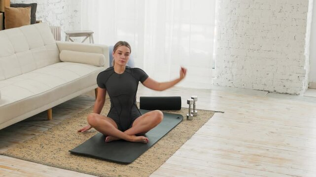 Sporty attractive woman practicing yoga, working out alone, wearing elegant sportswear on the mat in light room, near the white sofa. Active lifestyle.