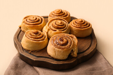 Board with tasty cinnamon rolls on light background