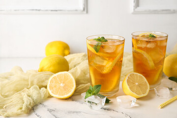 Lemons, ice cubes and glasses of tasty cold ice tea near white wall