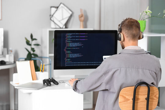 Male programmer with headphones working at table in office, back view