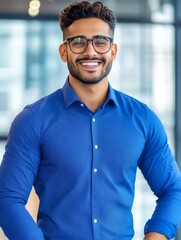 Obraz premium Indian Office Employee Smart Casual Shirt Coworking - A smiling Indian man in a blue shirt, embodying professionalism, success, collaboration