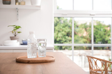 Bottle of water with glass on table in kitchen, closeup
