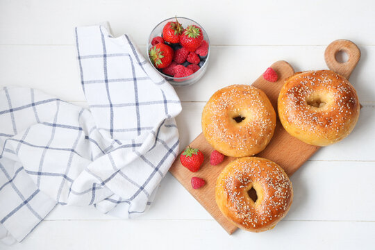 Board with tasty bagels and fresh berries on white wooden background