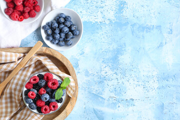 Glass of tasty yogurt with different fresh berries and mint on light blue background
