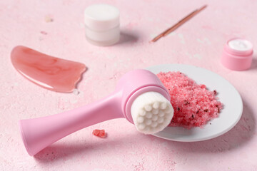 Facial massage brush and saucer with sea salt on pink background, closeup